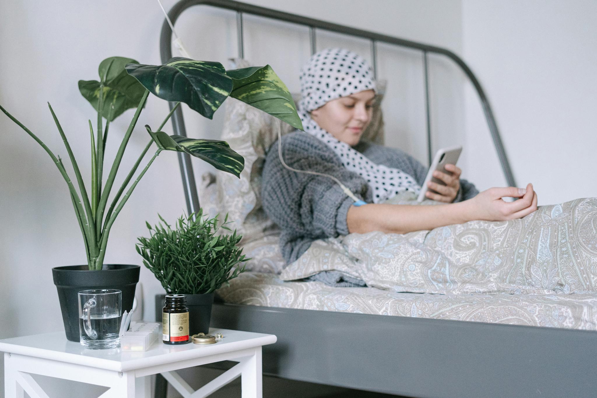 Our Mission A woman undergoing cancer treatment relaxes in bed using her phone, surrounded by plants.