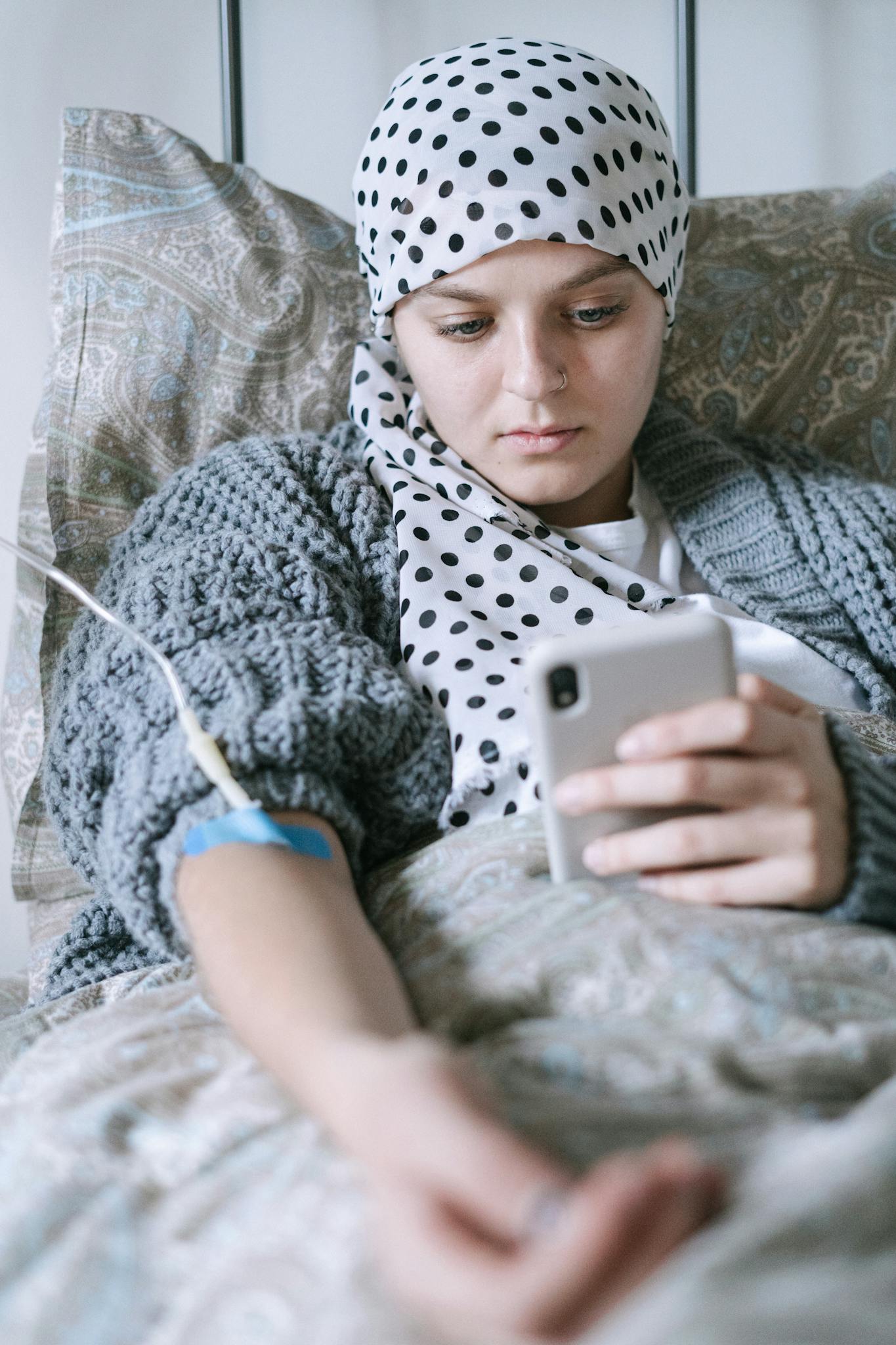 A young woman in bed receiving chemotherapy, using her phone for support.